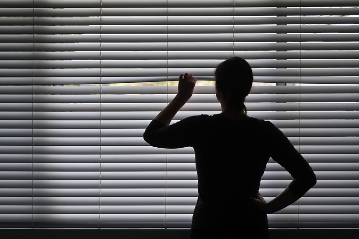 A woman seen from behind peeking out of window blinds